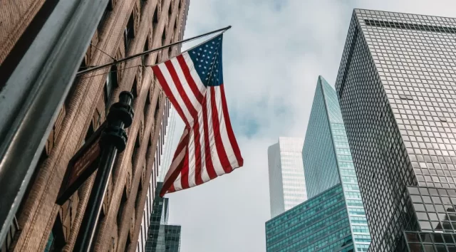a-bandeira-dos-eua-ou-estados-unidos-da-america-em-um-mastro-de-bandeira-perto-de-arranha-ceus-sob-um-ceu-nublado